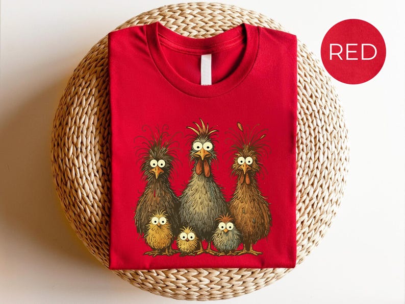 May include: A red t-shirt featuring a whimsical illustration of a chicken family. The design includes three adult chickens and three chicks, all with expressive eyes and detailed feathering. The word "RED" is in a red circle.