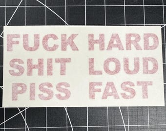 May include: Rectangular sticker with the words "FUCK HARD SHIT LOUD PISS FAST" printed in red. The sticker is on a white background, with a black grid pattern visible in the background.