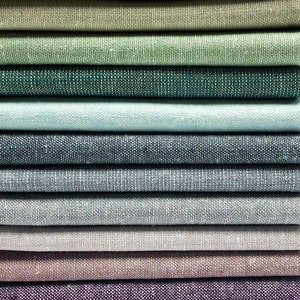 Puede incluir: Una pila de muestras de tela en varios tonos de verde, azul, gris y marr&oacute;n. La tela tiene una textura sutil y una apariencia similar al lino.