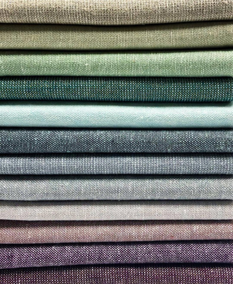 Puede incluir: Una pila de muestras de tela en varios tonos de verde, azul, gris y marr&oacute;n. La tela tiene una textura sutil y una apariencia similar al lino.