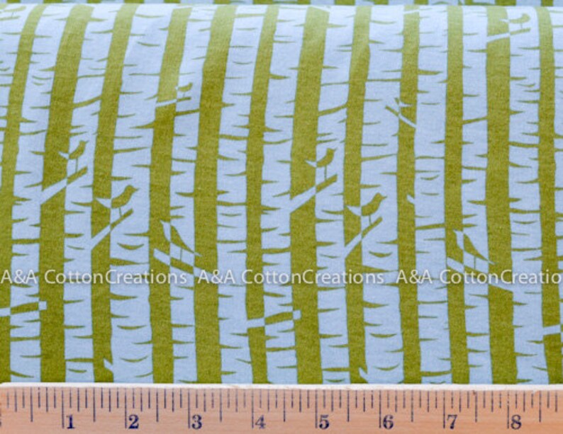 May include: A white fabric with a repeating pattern of green vertical stripes and small white birds on branches. The fabric is measured with a ruler in inches.