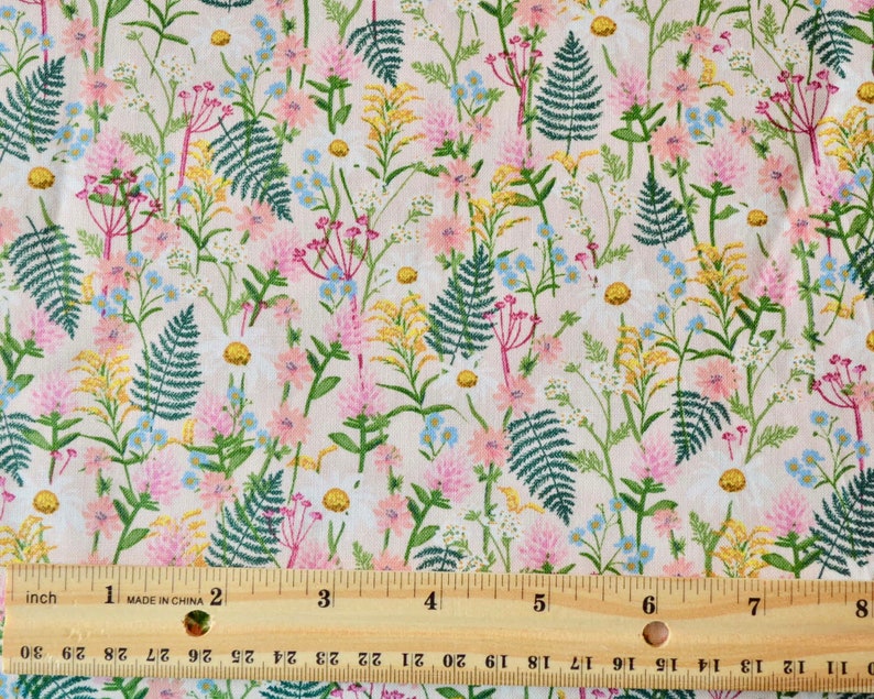 K&ouml;nnte beinhalten: Ein rosa-wei&szlig;er Stoff mit einem sich wiederholenden Muster aus gr&uuml;nen Farnen, rosa Bl&uuml;ten und gelben Wildblumen. Ein Lineal ist zur Gr&ouml;&szlig;enbestimmung im Bild enthalten.