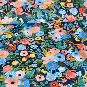 Puede incluir: Tela con un denso estampado floral sobre fondo azul marino. Presenta flores rosas, azules, amarillas y rojas, as&iacute; como hojas verdes. Las flores var&iacute;an en tama&ntilde;o y estilo.