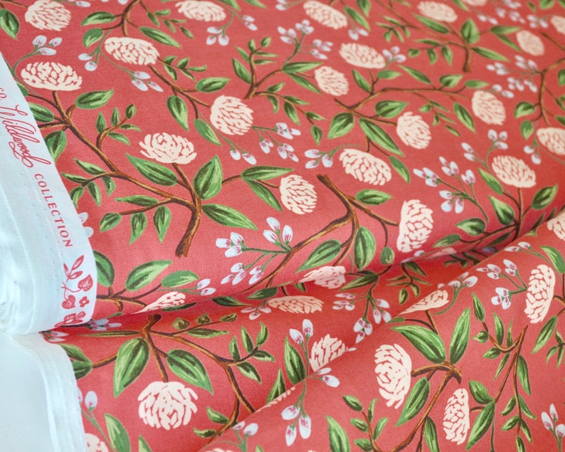 May include: Red fabric with a white floral pattern. The fabric features a repeating pattern of white peonies and green leaves on a red background. The fabric is labeled "Willowood Collection".