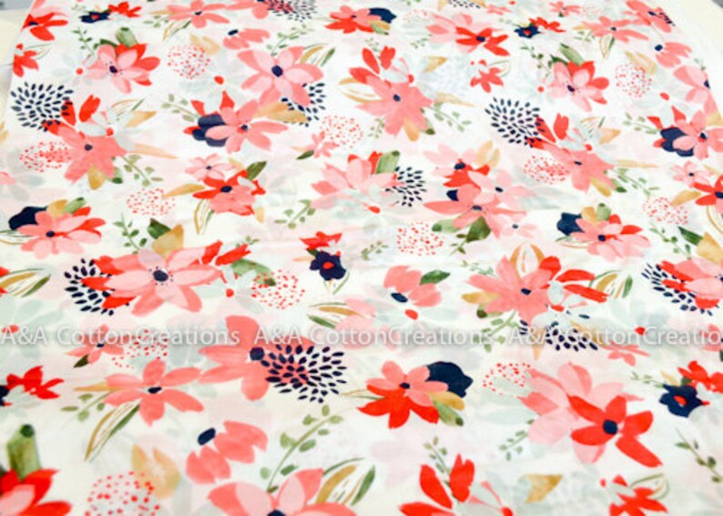 May include: White fabric with a pink and red floral print. The flowers are stylized and have a watercolor effect. The background is a light cream color.