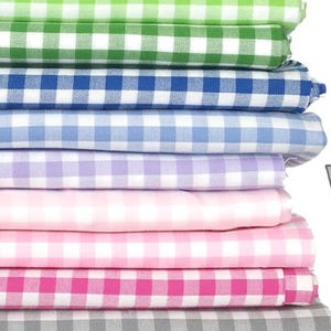 May include: A stack of 10 different colored gingham fabrics. The fabrics are folded and stacked on top of each other. The colors are red, yellow, green, blue, light blue, purple, pink, hot pink, gray, and black.