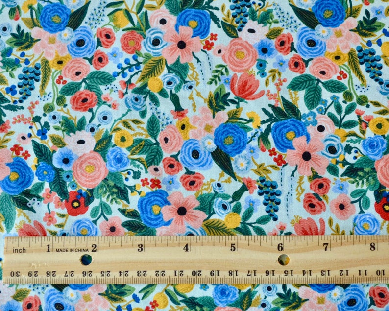 Puede incluir: Una tela azul claro con un patr&oacute;n floral con flores rosas, rojas, amarillas y azules. La tela se mide con una regla en pulgadas.