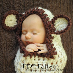 May include: A white crocheted baby sleeping bag with brown crocheted bear ears and a hood. The sleeping bag has a scalloped edge. The text "PDF Pattern" is visible at the bottom of the image.