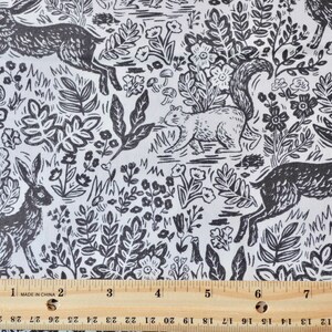 K&ouml;nnte beinhalten: Schwarz-wei&szlig;er Stoff mit einem Waldmuster, das Hasen, ein Eichh&ouml;rnchen, Blumen und Bl&auml;tter zeigt. Das Muster wiederholt sich. Ein Zoll-Lineal ist am unteren Rand zu sehen.