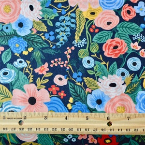 Puede incluir: Tela floral con fondo azul marino. La tela presenta un denso estampado de flores en tonos rosa, azul, amarillo y verde. Una regla de madera con medidas en pulgadas est&aacute; colocada sobre la tela.