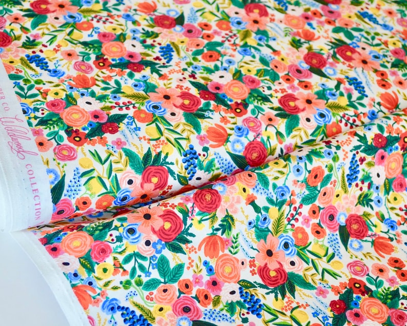 May include: Floral fabric with a white background and a colorful pattern of red, pink, blue, and yellow flowers. The fabric is from the Wildwood Collection.