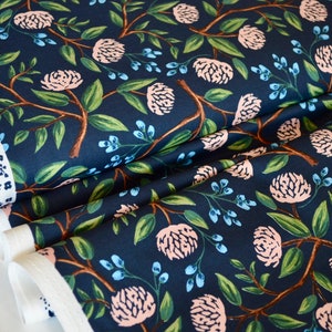 May include: Navy blue fabric with a repeating pattern of pink flowers, green leaves, and blue berries. The fabric is folded in thirds, showing the pattern from different angles.