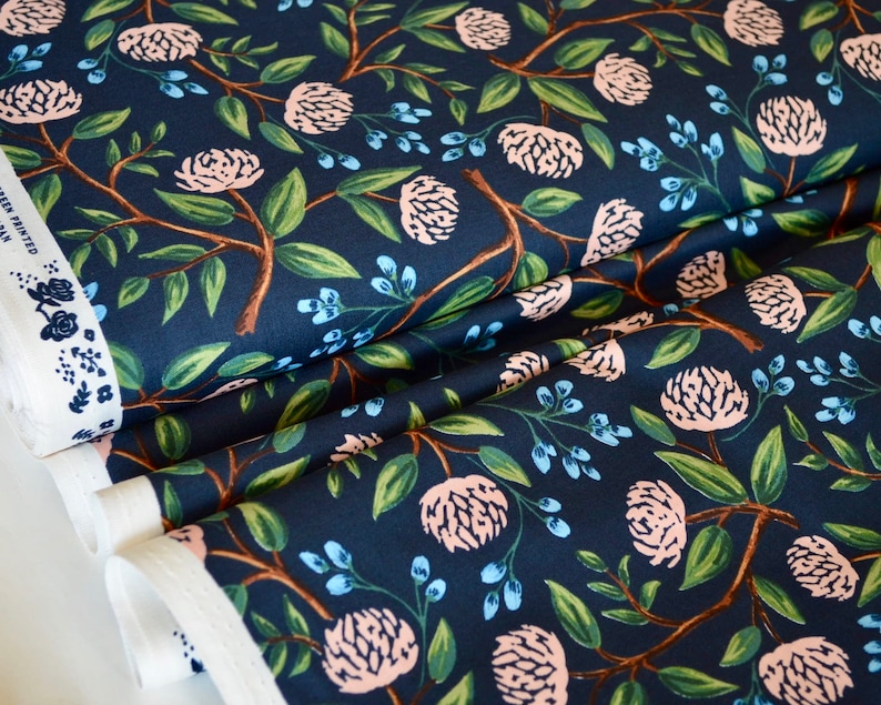May include: Navy blue fabric with a repeating pattern of pink flowers, green leaves, and blue berries. The fabric is folded in thirds, showing the pattern from different angles.