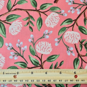 May include: Pink fabric with a white floral pattern. The fabric features large white flowers with green leaves and smaller white flowers with light blue centers. A ruler is placed at the bottom of the image for scale.