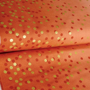 Könnte beinhalten: Orangener Stoff mit einem goldenen Konfetti-Muster. Der Stoff ist in der Mitte gefaltet, sodass das Muster auf beiden Seiten sichtbar ist.