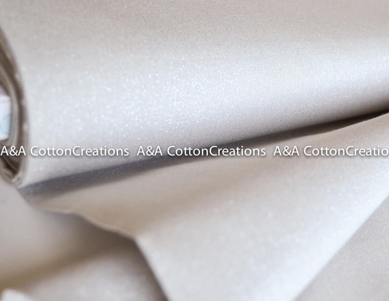 May include: A close-up of a roll of white fabric with a subtle sparkle. The fabric is folded in half and the edges are visible. The text "A&A Cotton Creations" is visible on the fabric.