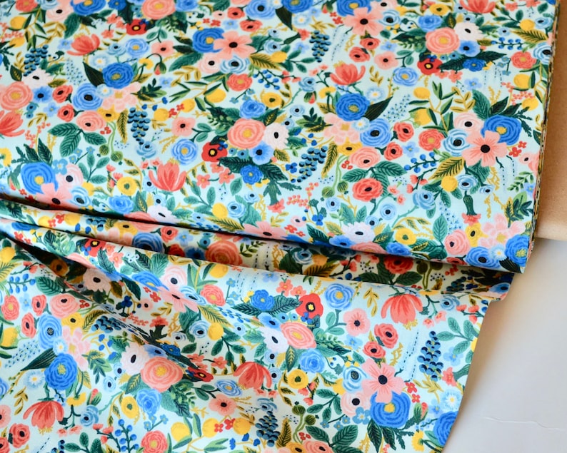 Puede incluir: Una tela azul claro con un patr&oacute;n floral. La tela presenta una variedad de flores en tonos de rosa, rojo, azul, amarillo y verde. Las flores est&aacute;n dispuestas en un patr&oacute;n aleatorio y est&aacute;n rodeadas de hojas y tallos.