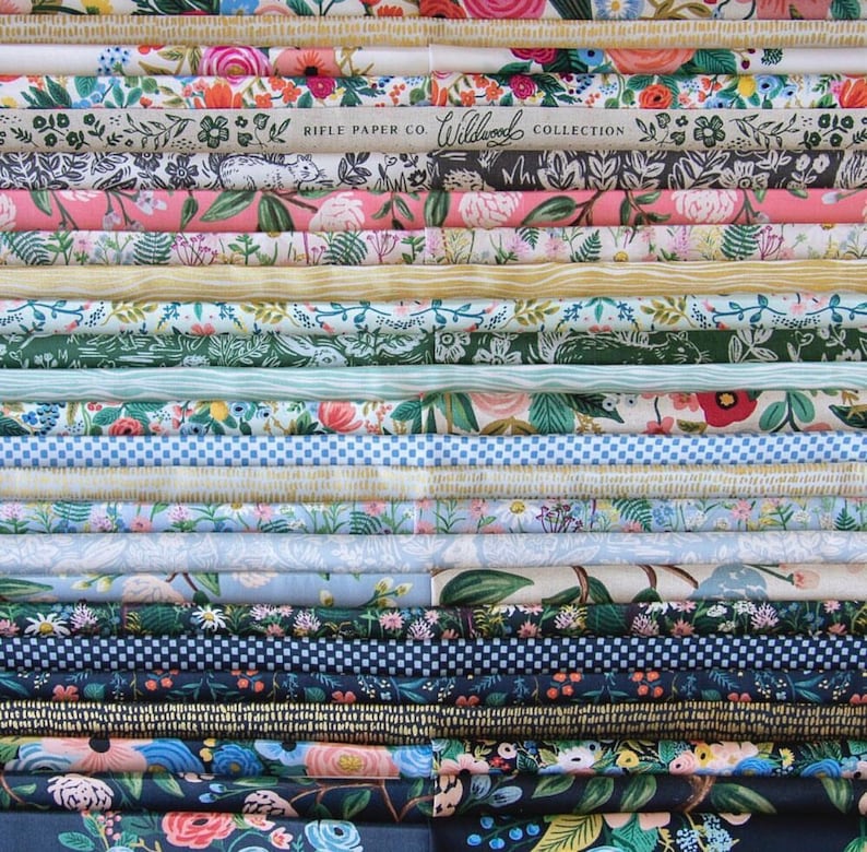 May include: A stack of colorful fabric featuring floral patterns and the text "Rifle Paper Co. Wildwood Collection".