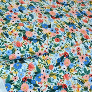 Puede incluir: Una tela azul claro con un patr&oacute;n floral con flores rosas, rojas, amarillas y azules. La tela est&aacute; cubierta con un patr&oacute;n denso de flores y hojas.