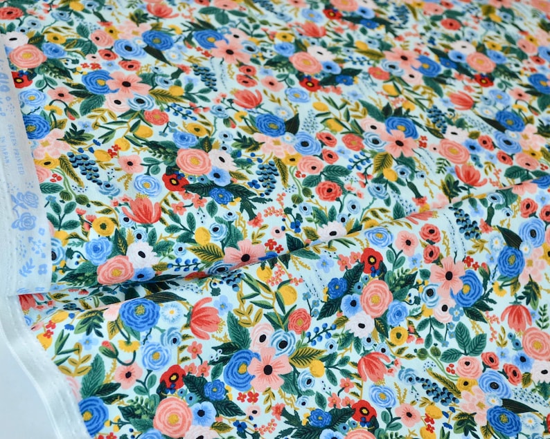 Puede incluir: Una tela azul claro con un patr&oacute;n floral con flores rosas, rojas, amarillas y azules. La tela est&aacute; cubierta con un patr&oacute;n denso de flores y hojas.