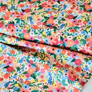 May include: Floral fabric with a dense pattern of colorful flowers. The design features red, pink, orange, yellow, and blue blooms with green leaves on a white background. The fabric is folded, showing the pattern's repeat.