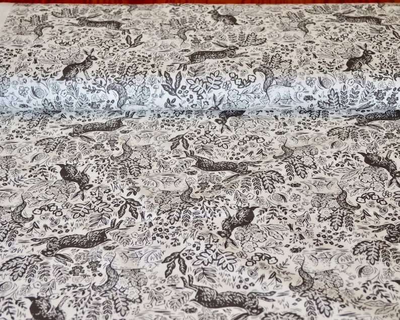 K&ouml;nnte beinhalten: Wei&szlig;er Stoff mit einem sich wiederholenden Muster aus schwarzen Hasen, V&ouml;geln, Eichh&ouml;rnchen, Schnecken und Bl&auml;ttern. Das Design zeigt detaillierte Illustrationen von Waldtieren und Pflanzen und schafft eine skurrile und von der Natur inspirierte &Auml;sthetik.