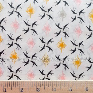 May include: White fabric with a repeating pattern of black birds, pink and yellow starbursts. The fabric is measured with a ruler in inches.