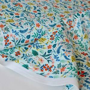 May include: A teal fabric with a floral pattern featuring small pink, red, and blue flowers with green leaves. The fabric is folded and rolled up.