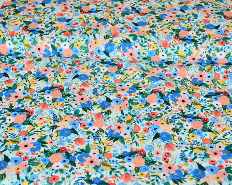 Puede incluir: Una tela azul claro con un patr&oacute;n floral con flores rosas, azules, amarillas y verdes. La tela est&aacute; cubierta con un patr&oacute;n denso de flores.