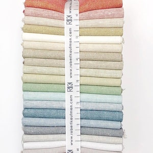 Puede incluir: Un conjunto de 20 muestras de tela en varios tonos de melocot&oacute;n, beige, verde, azul y gris. Las muestras de tela est&aacute;n atadas con una cinta blanca que tiene el texto "RIK www.robertkaufman.com" impreso en ella.