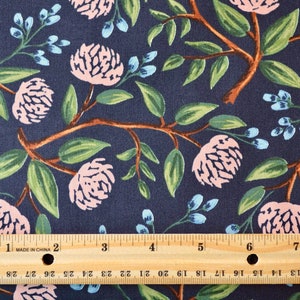 May include: A navy blue fabric with a repeating pattern of pink flowers and green leaves. A wooden ruler with inch markings is placed on top of the fabric.