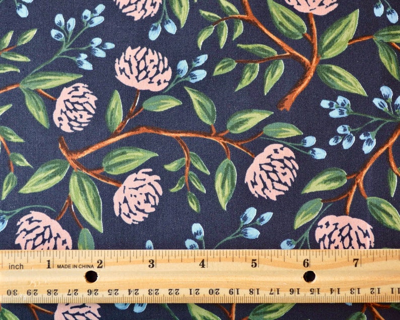May include: A navy blue fabric with a repeating pattern of pink flowers and green leaves. A wooden ruler with inch markings is placed on top of the fabric.