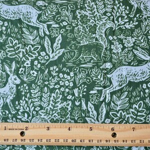 Puede incluir: Tela verde con un estampado blanco de bosque con conejos, ardillas, flores y follaje. El dise&ntilde;o se repite en la tela. Una regla con medidas en pulgadas est&aacute; en la parte inferior de la imagen.