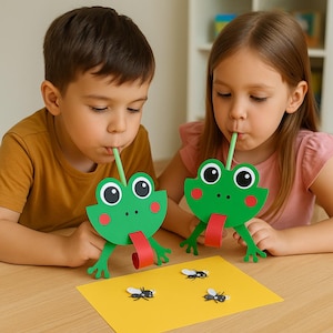 Puede incluir: Dos niños juegan con marionetas de rana de papel verde. Las marionetas tienen lenguas rojas y ojos blancos grandes. Usan pajitas verdes para jugar con moscas de papel sobre una superficie amarilla. Las ranas tienen mejillas rojas.