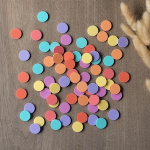Könnte beinhalten: Eine Ansammlung bunter, runder Spielsteine in Orange, Rot, Gelb, Lila und Türkis auf einer Holzoberfläche. Die Teile sind in einem zufälligen Muster angeordnet, was auf ein Spiel oder eine Bastelaktivität hindeutet.