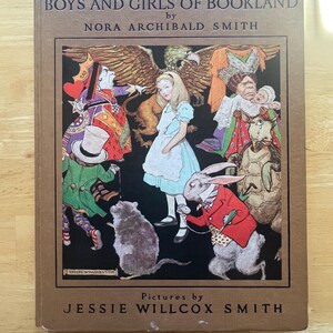 Pode incluir: Um livro vintage de capa dura intitulado "Boys and Girls of Bookland" de Nora Archibald Smith, com ilustrações de Jessie Willcox Smith. A capa apresenta uma ilustração colorida de personagens de Alice no País das Maravilhas.