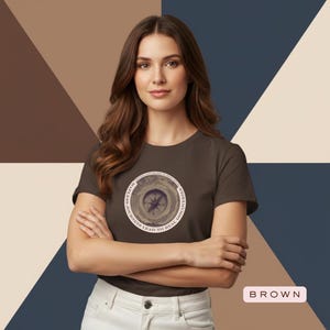 May include: A brown t-shirt featuring a circular graphic with a compass design and the text "Mapless Journeys Lead to Real Discoveries." The shirt is paired with white pants. The word "BROWN" is displayed in a rectangular box.
