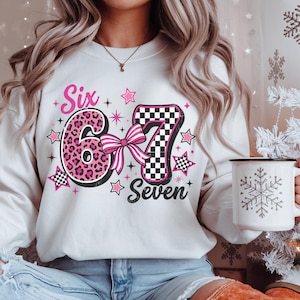 May include: White sweatshirt with a pink and black graphic that says "Six 6 Seven" with stars and a bow. The number 6 has a pink leopard print design, and the number 7 has a black and white checkered pattern.
