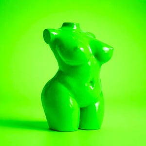 Könnte beinhalten: Eine glänzende, limettengrüne Skulptur eines weiblichen Torsos. Die Skulptur hat eine glatte, reflektierende Oberfläche und ist vor einem passenden grünen Hintergrund platziert. Die Form ist stilisiert, mit definierten Kurven und minimalistischer Ästhetik.