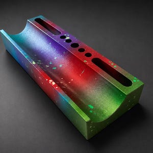 May include: A rectangular desk organizer with a curved trough and several circular and oblong openings. The organizer is painted with a gradient of colors, including blue, purple, red, and green, with paint splatters.