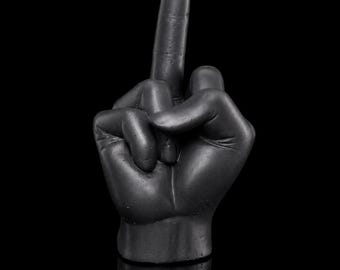 May include: A matte black sculpture of a hand with the middle finger extended in a gesture. The hand is positioned vertically with a flat base, showing detailed knuckles, skin texture, and fingernails in a solid, dark, monochromatic finish.