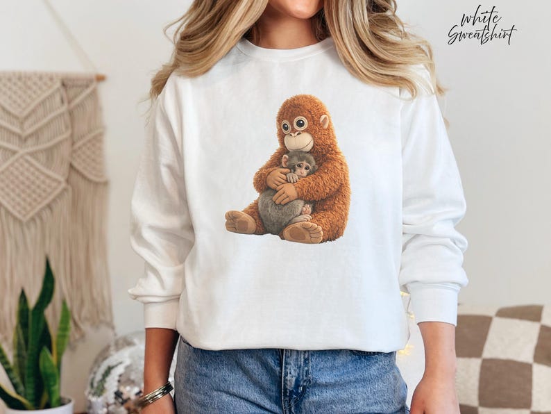 Puede incluir: Sudadera blanca con una ilustraci&oacute;n detallada de un orangut&aacute;n abrazando a un beb&eacute; mono. El orangut&aacute;n tiene pelaje marr&oacute;n y el beb&eacute; mono es gris. El texto "White Sweatshirt" est&aacute; en la esquina superior derecha.