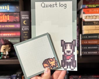 May include: A set of pixel art-style notepads with a light green background. One notepad reads "Quest log" in pixelated text. The other notepad features a pixelated dog and a person. The notepads are held in a person's hand.