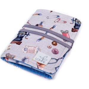 May include: A gray fabric sewing kit roll-up with a blue interior and gray elastic closure. The fabric is patterned with sewing machine illustrations, thimbles, needles, and buttons. A white label with the text "LOMME" is visible.