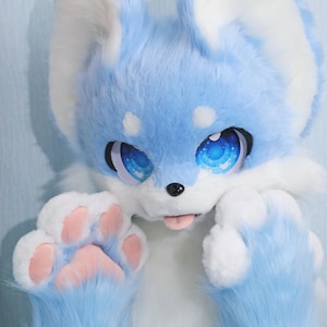 May include: A blue and white furry fox costume head with large, expressive blue eyes. The costume has a pink tongue sticking out and pink paw pads. The fur is a soft, plush material, creating a whimsical and playful appearance.