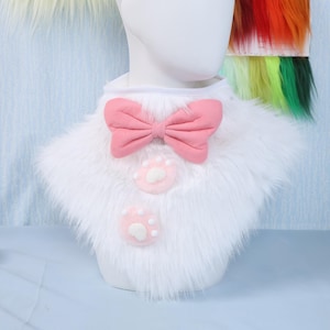 May include: A white faux fur collar with a pink bow and two pink paw print accents. The collar is designed to be worn around the neck. The bow is centered on the collar, and the paw prints are below the bow.