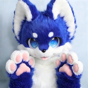 Op de afbeelding: Een pluche dierenkopmasker met levendig blauw en wit imitatiebont, grote expressieve blauwe ogen met een sterrenpatroon, puntige oren en een kleine zwarte neus. Het masker bevat bijpassende blauw-witte harige poten met zachte roze kussentjes.