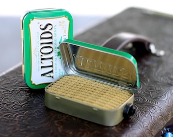 May include: An Altoids mint tin, green in colour, with the text "The Original Celebrated Altoids Curiously Strong Mints" on the front. The tin is open and the inside is empty.