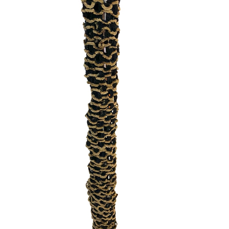 May include: A vertical close-up of a decorative item with a repeating pattern. The item is a column of alternating black and tan, looped, textured material. The background is plain white.