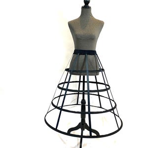 May include: A black, circular, multi-tiered cage skirt with a black ribbon waistband. The skirt is on a gray dress form.